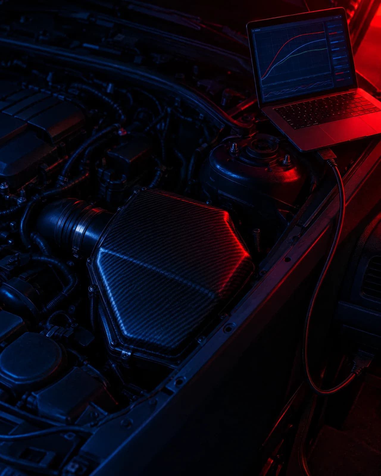 An engine bay with an enclosed airbox fitted and a laptop showing a tuning graph on the strut tower