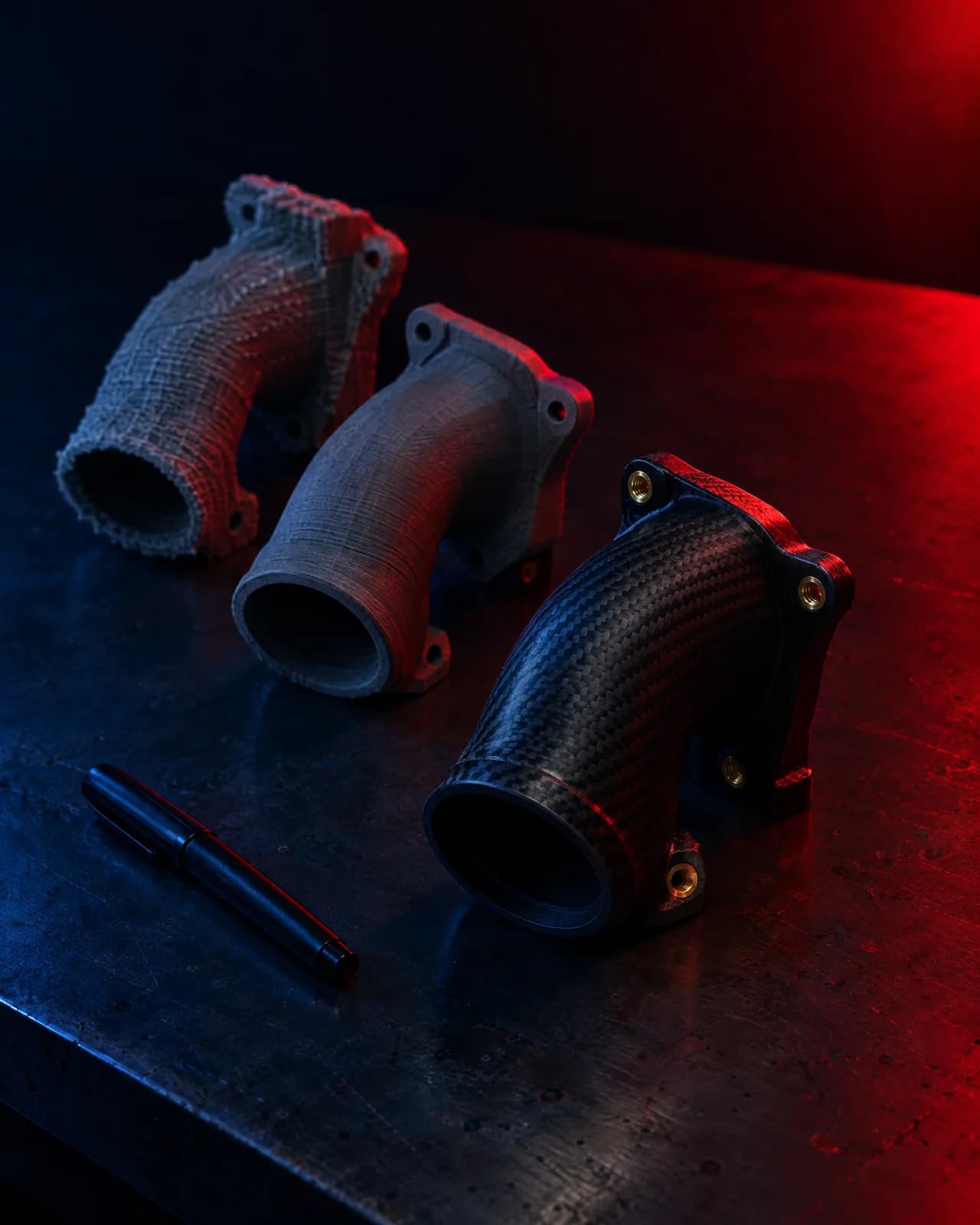 Three iterations of a printed intake part lined up on a bench, each a step closer to final