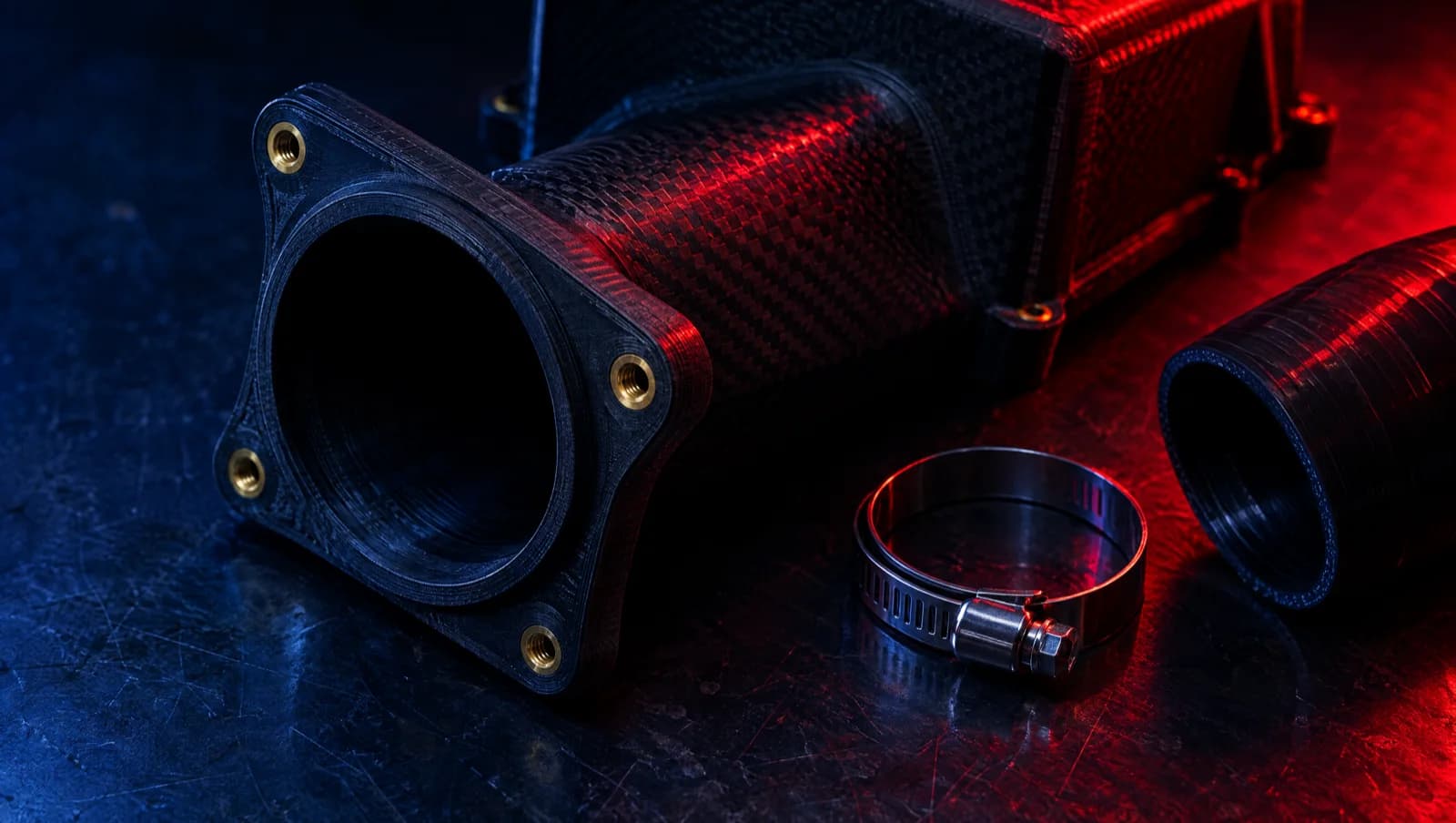 Black carbon-fibre printed airbox flange with brass inserts, a hose clamp and a flexible pipe on a steel bench