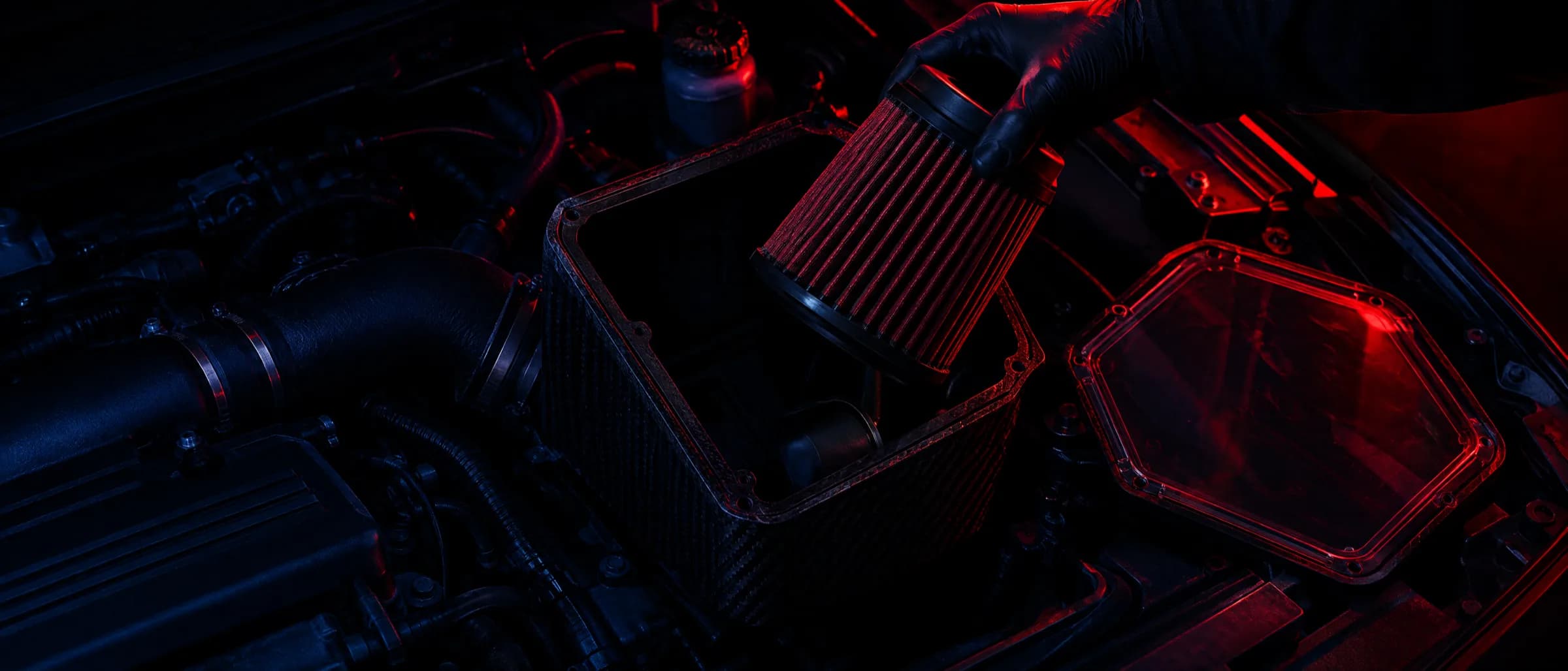 A gloved hand lifting the filter out of an open airbox in an engine bay